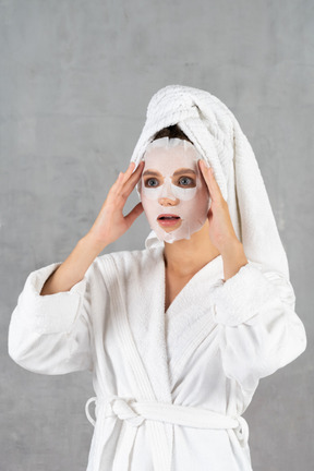 Woman in bathrobe looking surprised and touching temples