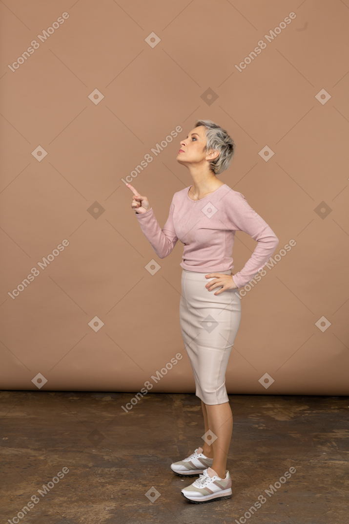 Vista lateral de uma mulher com roupas casuais apontando para cima com o dedo