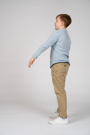 Vista lateral de um menino feliz em pé com o braço estendido
