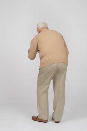 Rear view of an old man in casual clothes standing with outstretched arm and explaining something