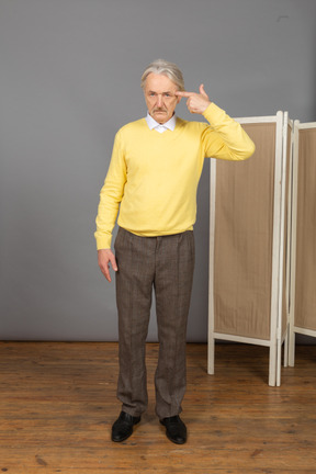 Vista frontal de um homem idoso pensativo em um pulôver amarelo apontando para a cabeça