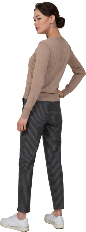 Vista posteriore di tre quarti di una donna furba in pullover e pantaloni che mette la mano sul fianco