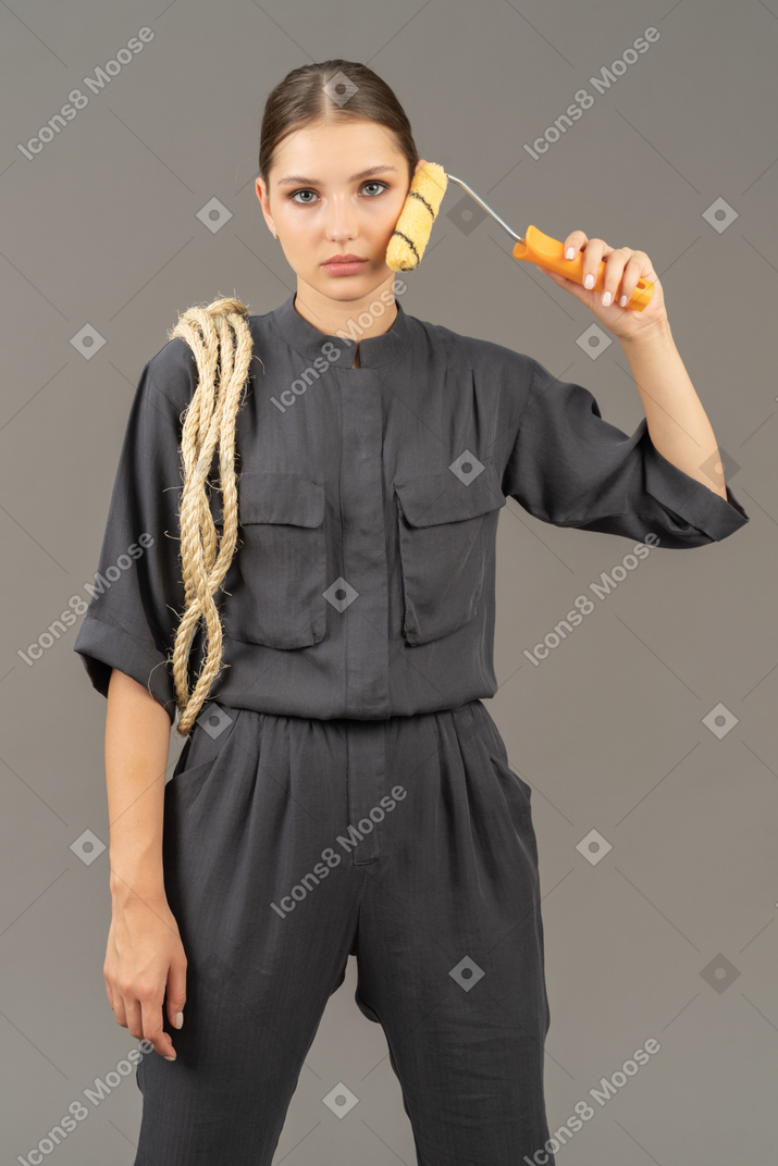 Woman in gray coveralls holding a paint roller to her cheek