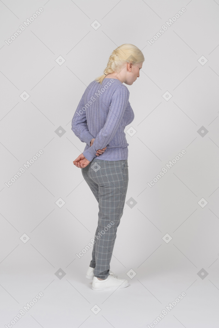 Mujer con las manos entrelazadas a la espalda caminando y mirando hacia abajo