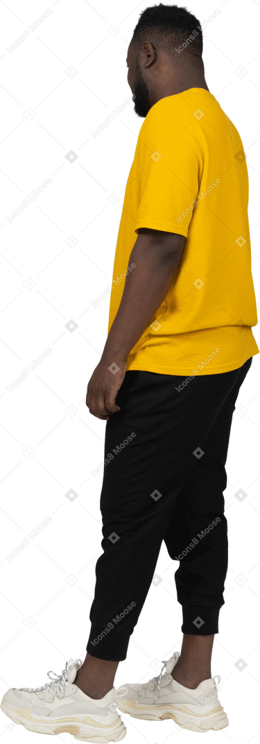 Vista posteriore di tre quarti di un giovane uomo dalla pelle scura in maglietta gialla che sta fermo