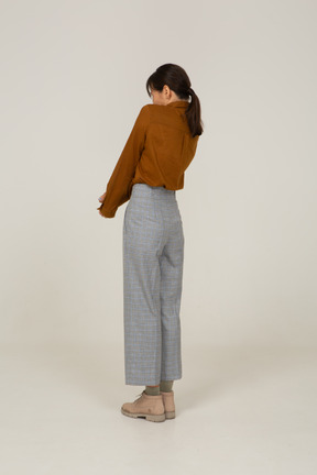 Vista posteriore di tre quarti di una giovane donna asiatica in calzoni e camicetta che si tiene per mano e si appoggia all'indietro