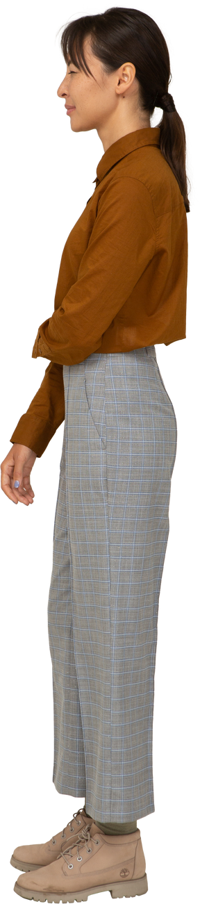 Vista lateral de uma jovem mulher asiática de calça e blusa estreitando os olhos