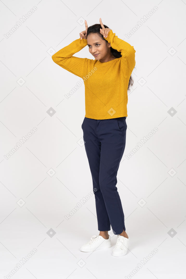 Front view of a happy girl in casual clothes making horns with fingers