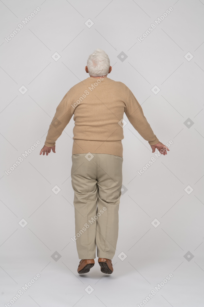 Rear view of an old man in casual clothes jumping