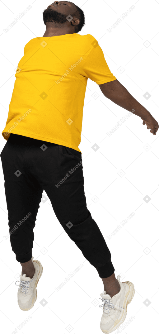 四分之三的视图，一个身穿黄色 t 恤、伸开双手的年轻深色皮肤男子跳跃