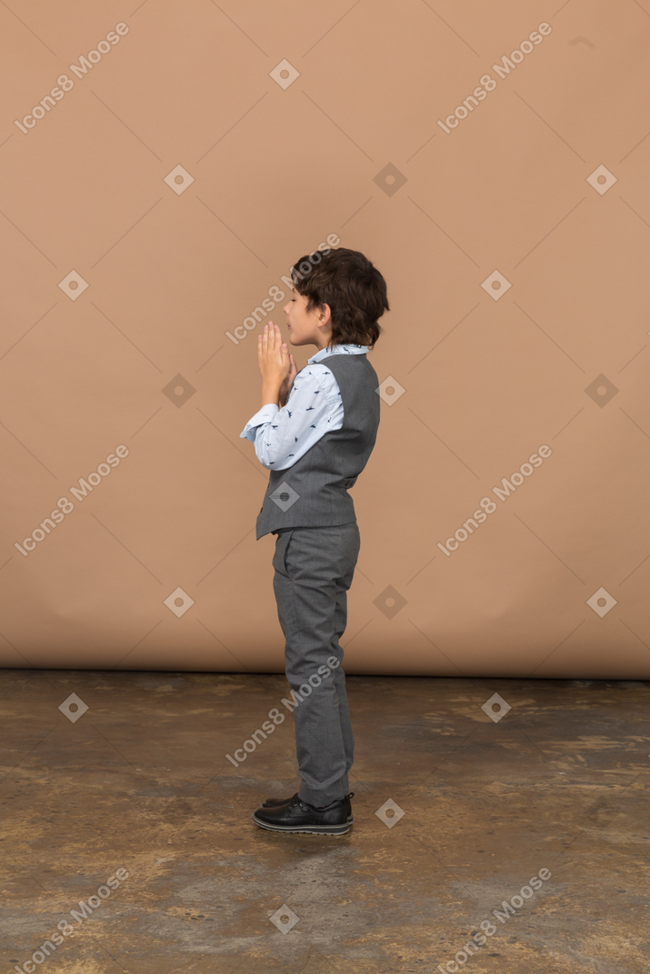 Vista lateral de un niño en traje haciendo gesto de oración