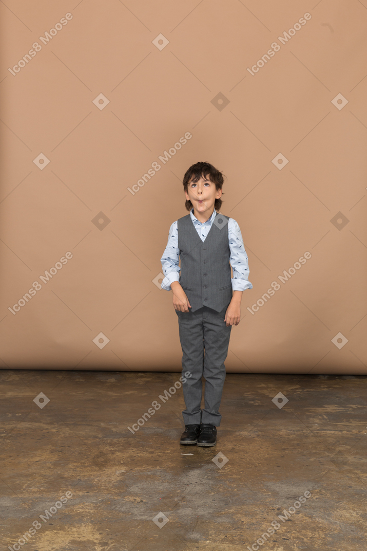 Vista frontal de un niño en traje parado y haciendo muecas