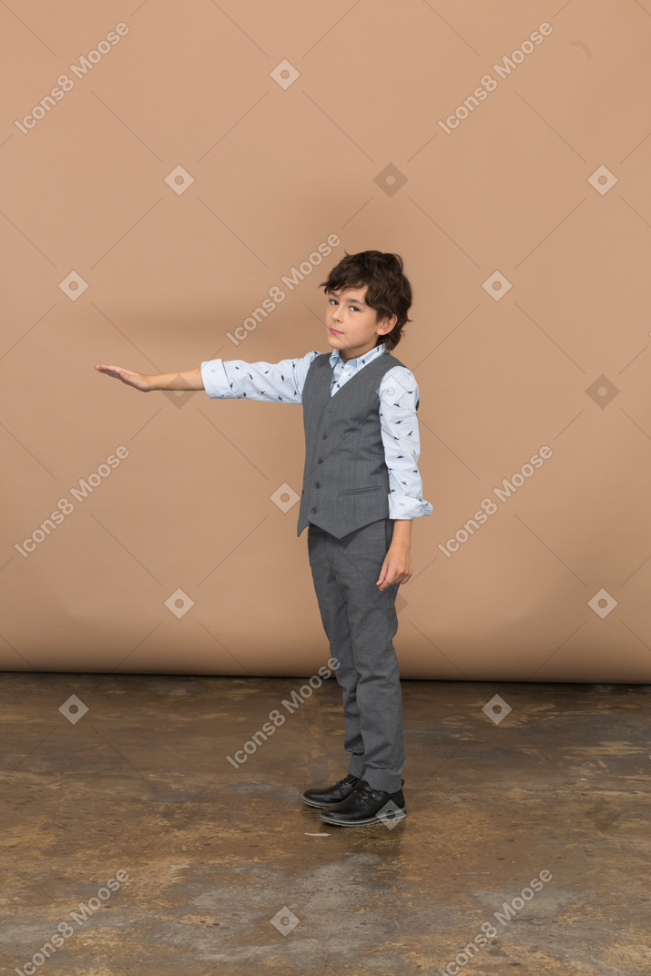 Вид сбоку мальчика в сером костюме, стоящего с протянутой рукой