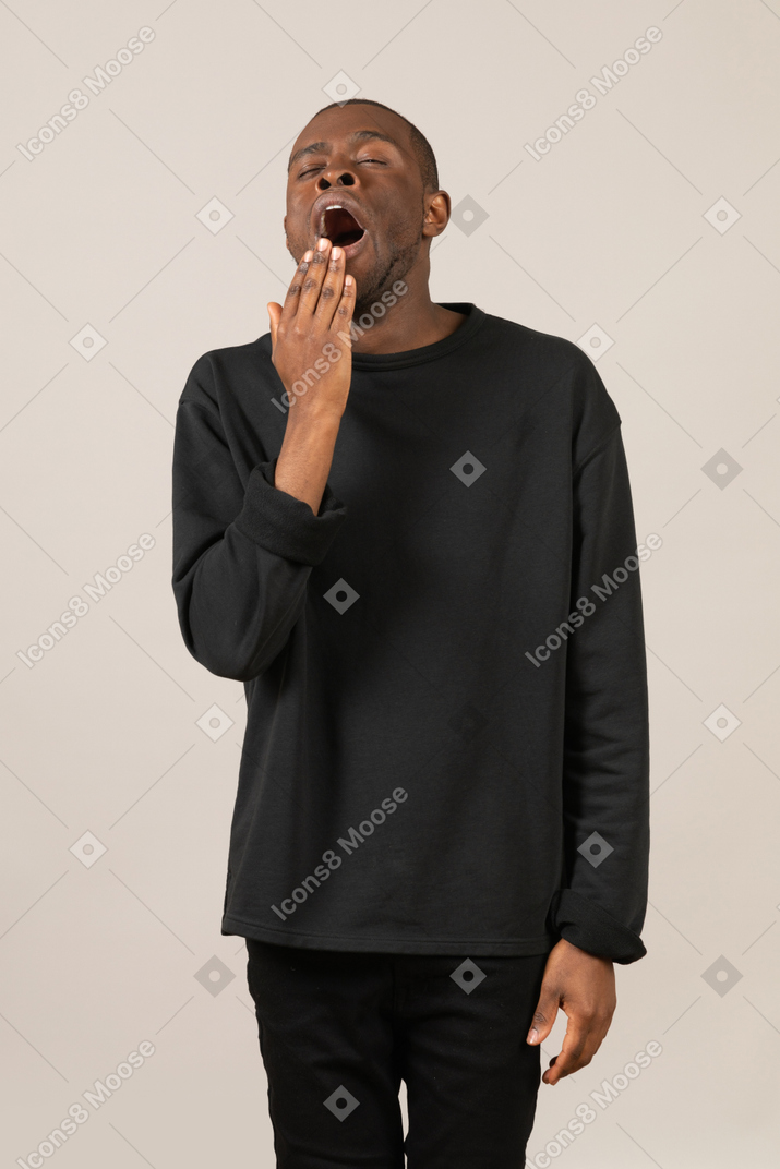 Man in black clothes yawning and covering his mouth