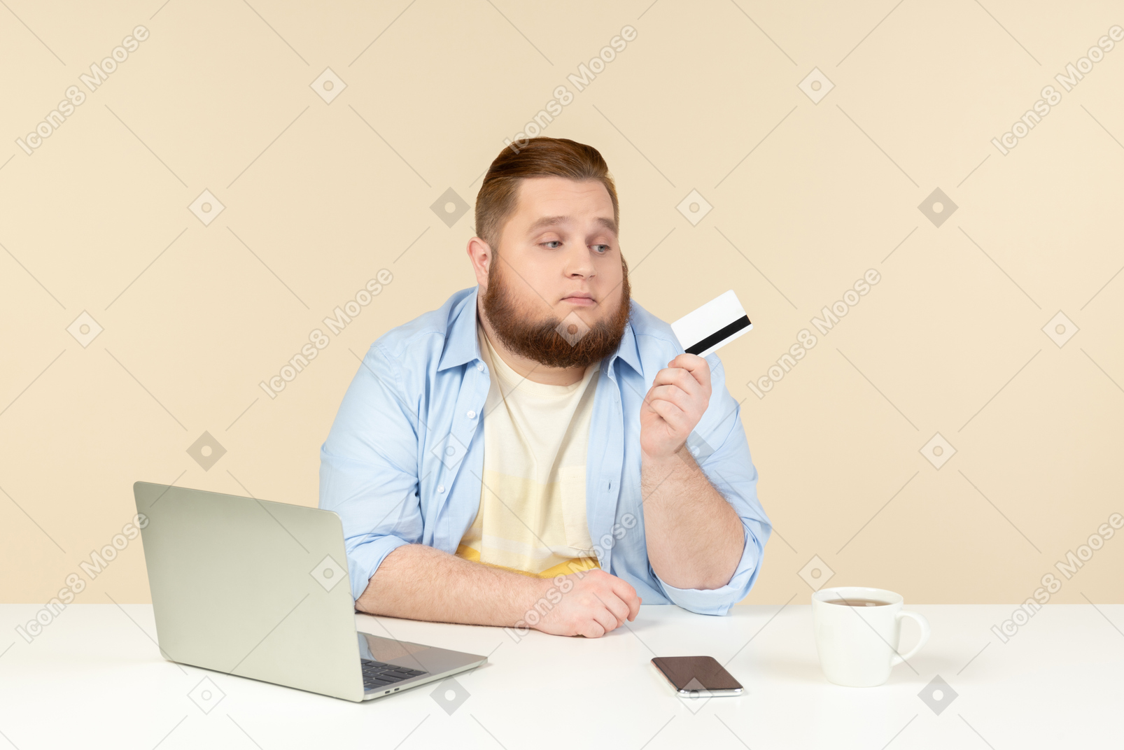 Sad looking young overweight man sitting at the desk and holding bank card