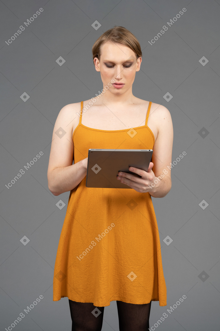Front view of a young queer person in orange dress using tablet