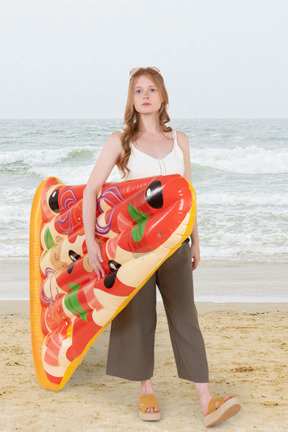 A woman standing on a beach with a pizza pool float