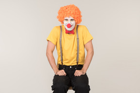 Male clown in red wig sitting on the chair