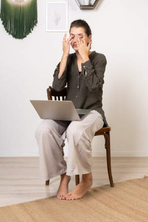 四分之三的视角是一位忙碌的年轻女性，头疼地坐在椅子上，拿着笔记本电脑