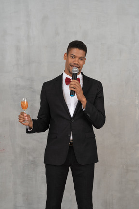 Man holding glass and mic and looking at camera