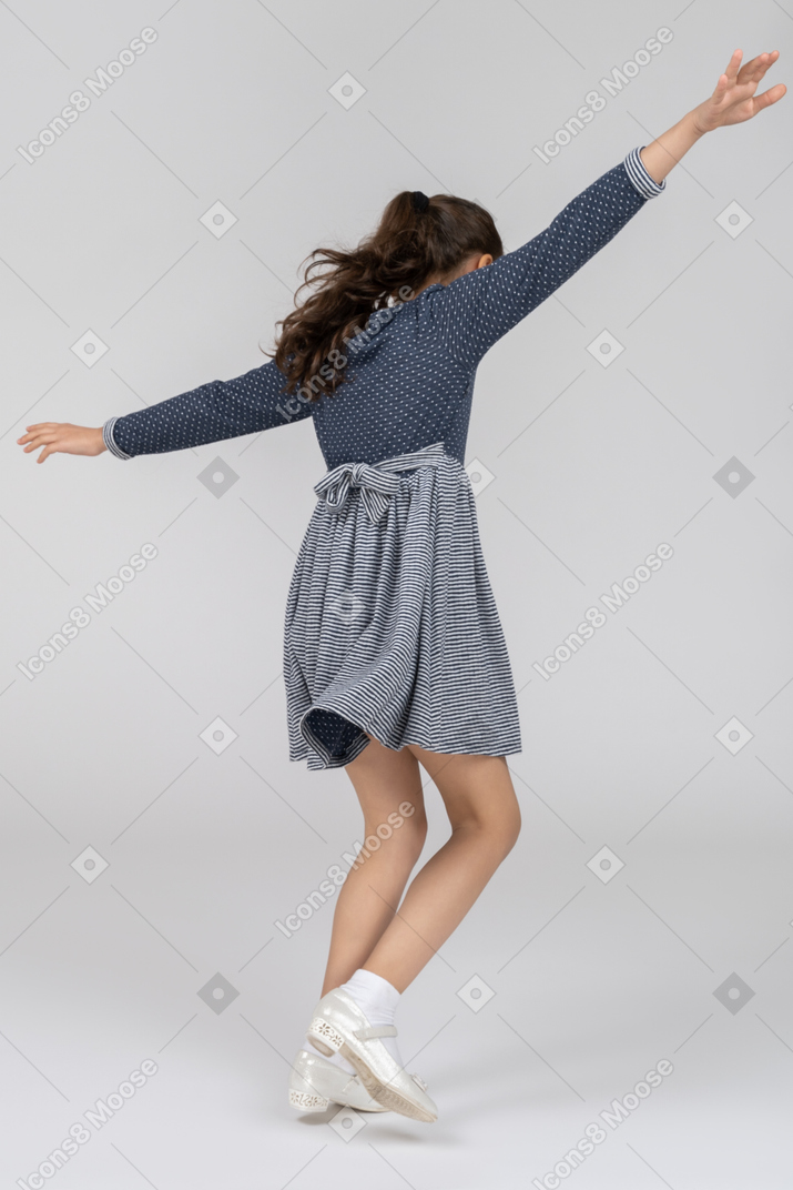 Vista traseira de três quartos de uma garota imitando voar como um avião