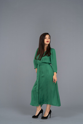 Three-quarter view of a proud young lady in green dress putting hand on hip