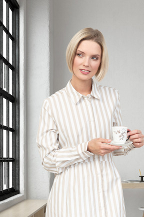 A woman in a striped shirt holding a cup and looking at window