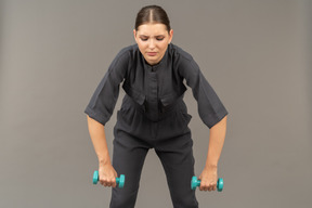 Front view of young woman in a jumpsuit doing exercises with dumbbells