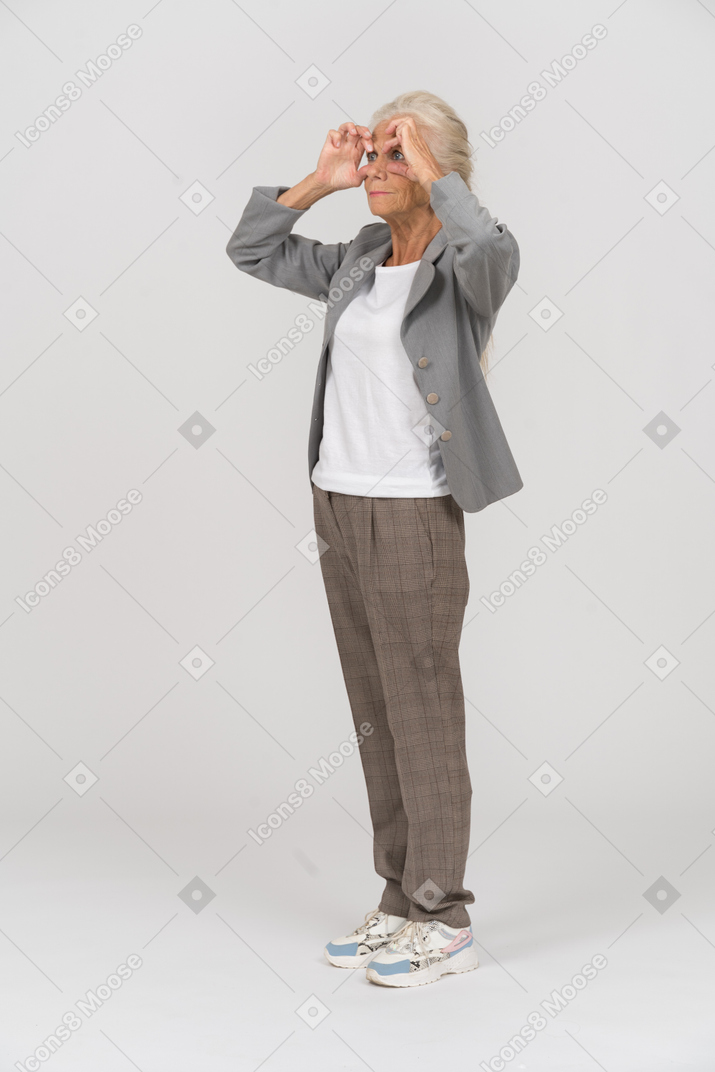 Vista lateral de una anciana en traje mirando a través de binoculares imaginarios