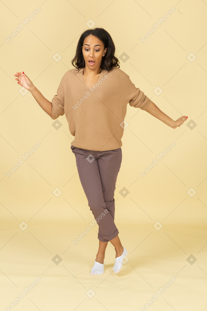 Vista frontal de una mujer joven asustada de piel oscura que camina extendiendo sus manos