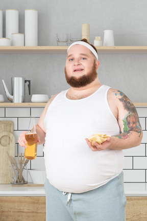 A man in a white tank top holding a bottle of beer and chips in his hand