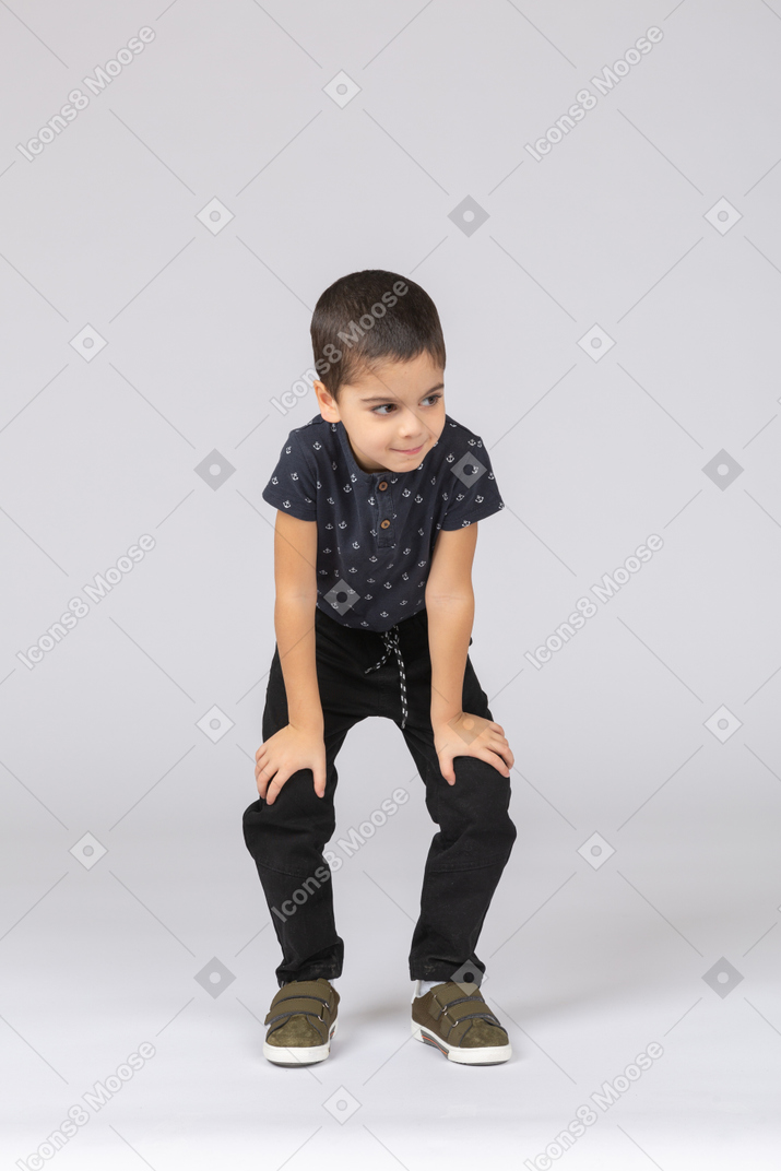 Вид спереди симпатичного мальчика, сидящего на корточках и смотрящего в камеру