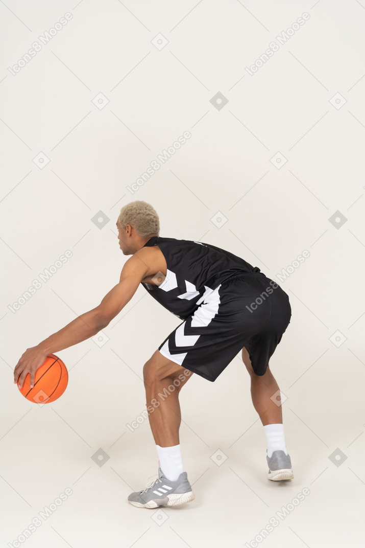 Vista posterior de tres cuartos de un joven jugador de baloncesto masculino haciendo regate