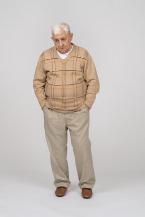 Front view of a sad old man in casual clothes standing with hands in pockets