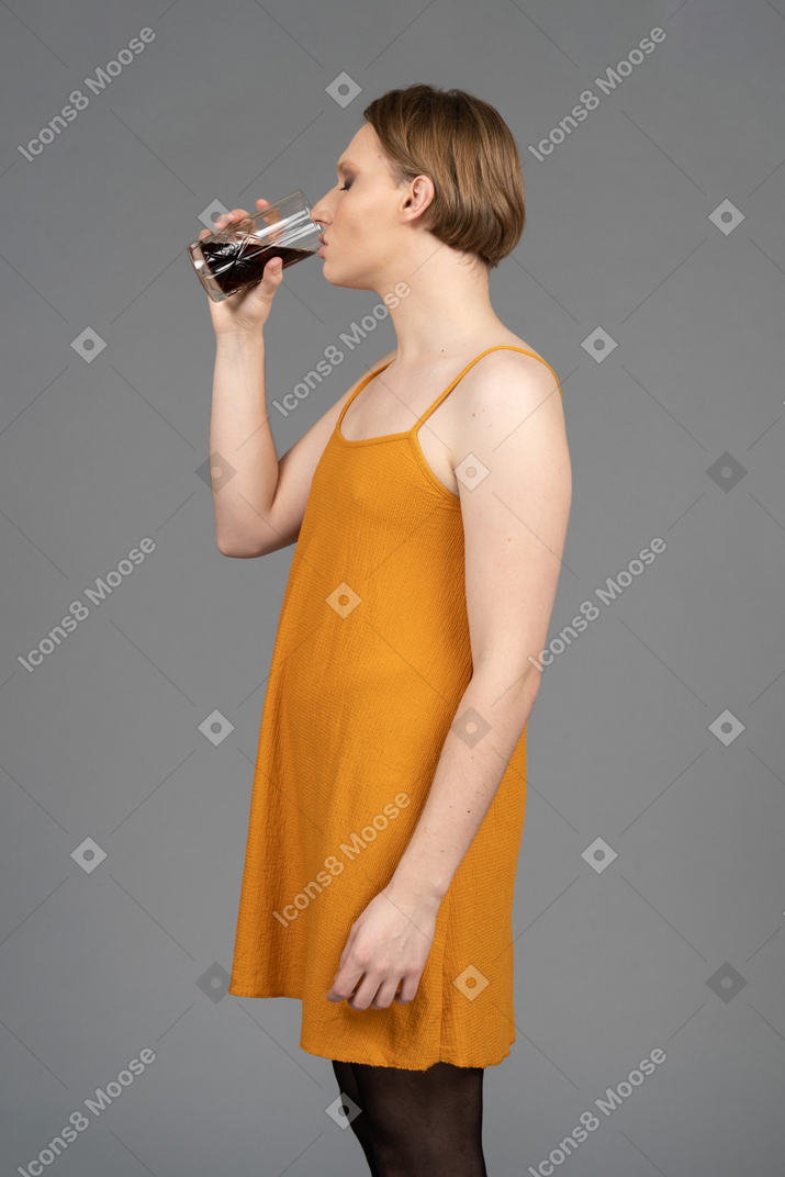 一个穿着橙色连衣裙的年轻非二元人喝一口的侧视图
