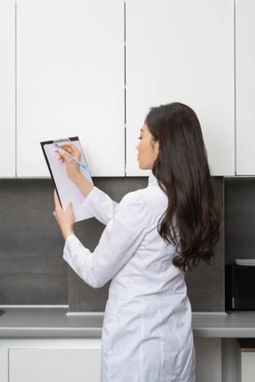 Three-quarter back view of a young female doctor raising hands and taking notes on her tablet