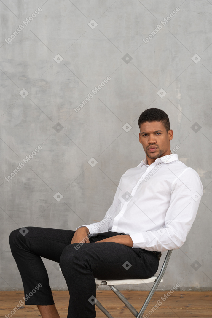 Молодой человек сидит на стуле и смотрит в камеру