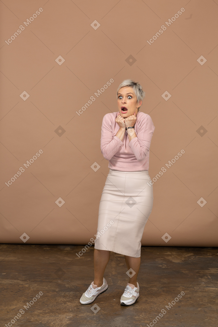 Вид спереди впечатленной женщины в повседневной одежде, касающейся кулаками подбородка