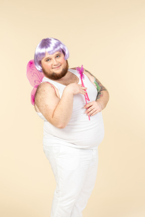 Young overweight man dressed as a fairy holding fairy wand and looking aside