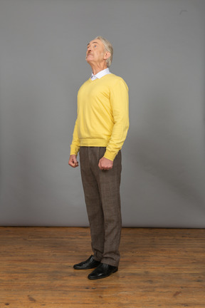 Трехчетвертный вид любопытного старика в желтом свитере, поднимающего голову и смотрящего вверх