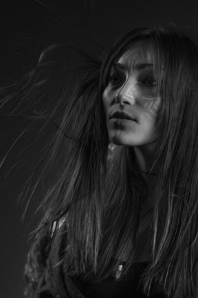 Noir three-quarter portrait of a young female with ethnic facial art and messy hair