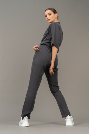 Three-quarter back view of a young woman in a jumpsuit making a step