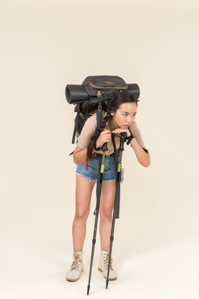 Tired young hiker woman standing with huge backpack and leaning on trekking poles