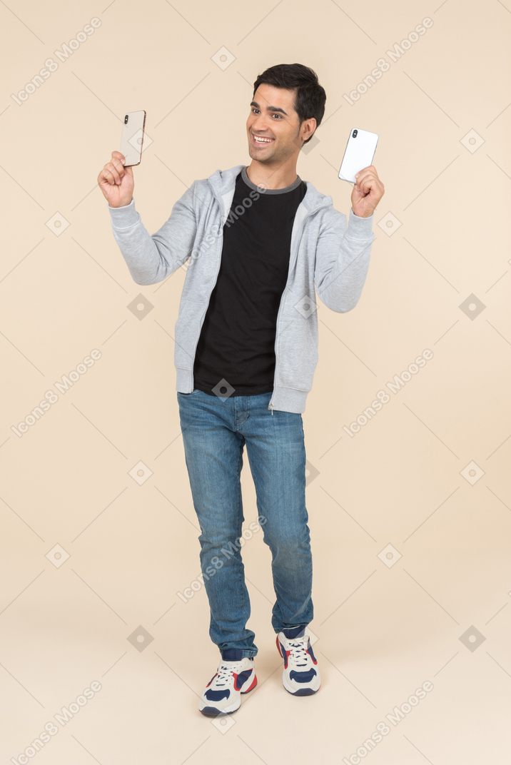 Laughing young caucasian man holding two smartphones