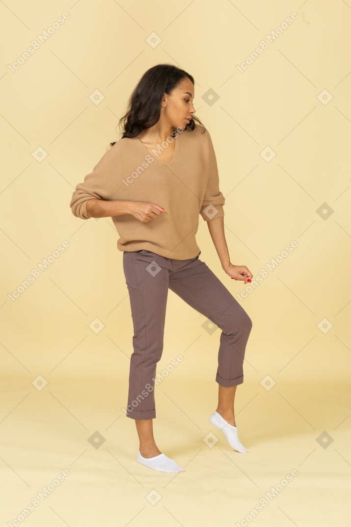 Front view of a dancing dark-skinned young female bending knee