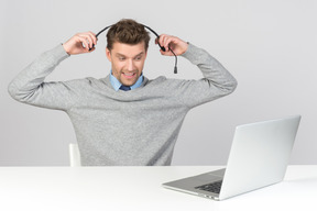 Call-center-agent zieht sein headset ab, während er am computer arbeitet