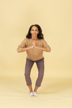 Front view of a squatting dark-skinned young female holding hands together