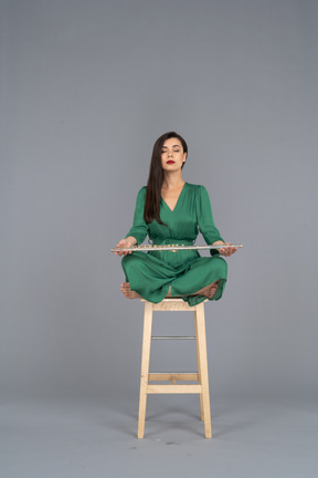 Full-length of a young lady holding her clarinet on her knees while sitting on a wooden chair