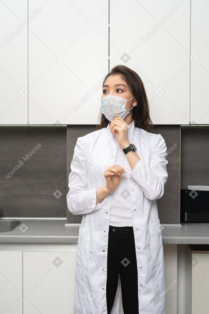 Vista frontale di una dottoressa che regola la sua maschera protettiva e che osserva da parte