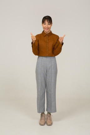 Vista frontal de una joven mujer asiática en calzones y blusa mostrando los pulgares hacia arriba